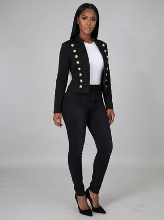 Angled view of a black gold-button military cropped jacket showing the stand collar, long fitted sleeves and waist-length cut