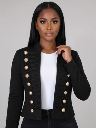 Close-up of a black military band jacket showing gold domed buttons, black cord frog trim and stand collar over a white top