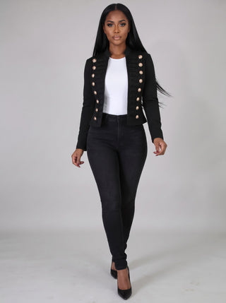 Model walking in a black cropped gold-button military jacket with a white top and black skinny jeans