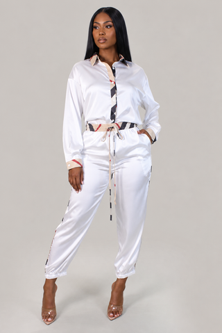 Woman in ivory satin button-front shirt and matching drawstring pants with tan and black check contrast trim, styled with clear heels